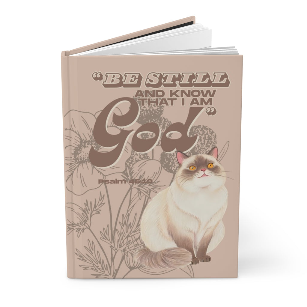 Notebook with a cat illustration and 'Be Still and Know That I Am God' text on a beige background