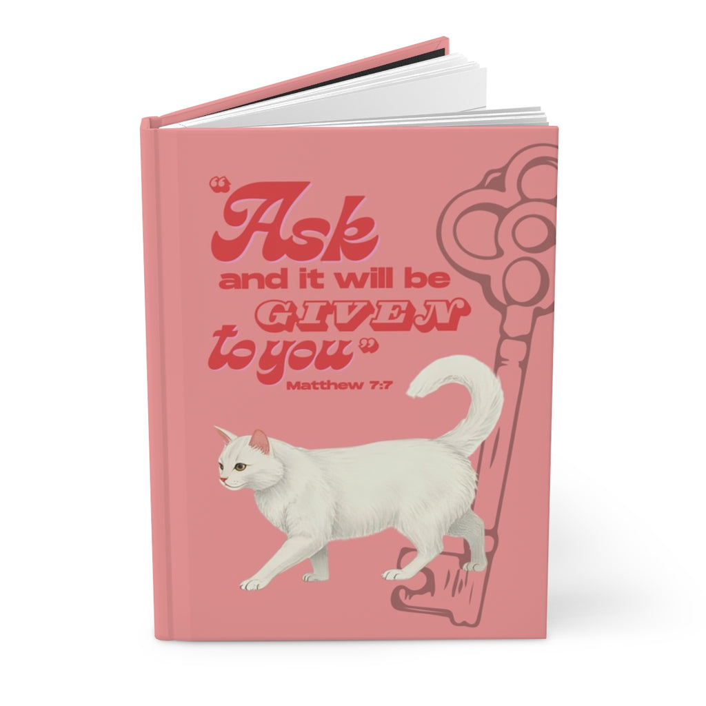 Pink book with a white cat illustration and motivational quote on a white background