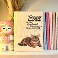 Yellow notebook with a brown tabby cat illustration and Psalm 23:1 text on a shelf with books and a decorative item.