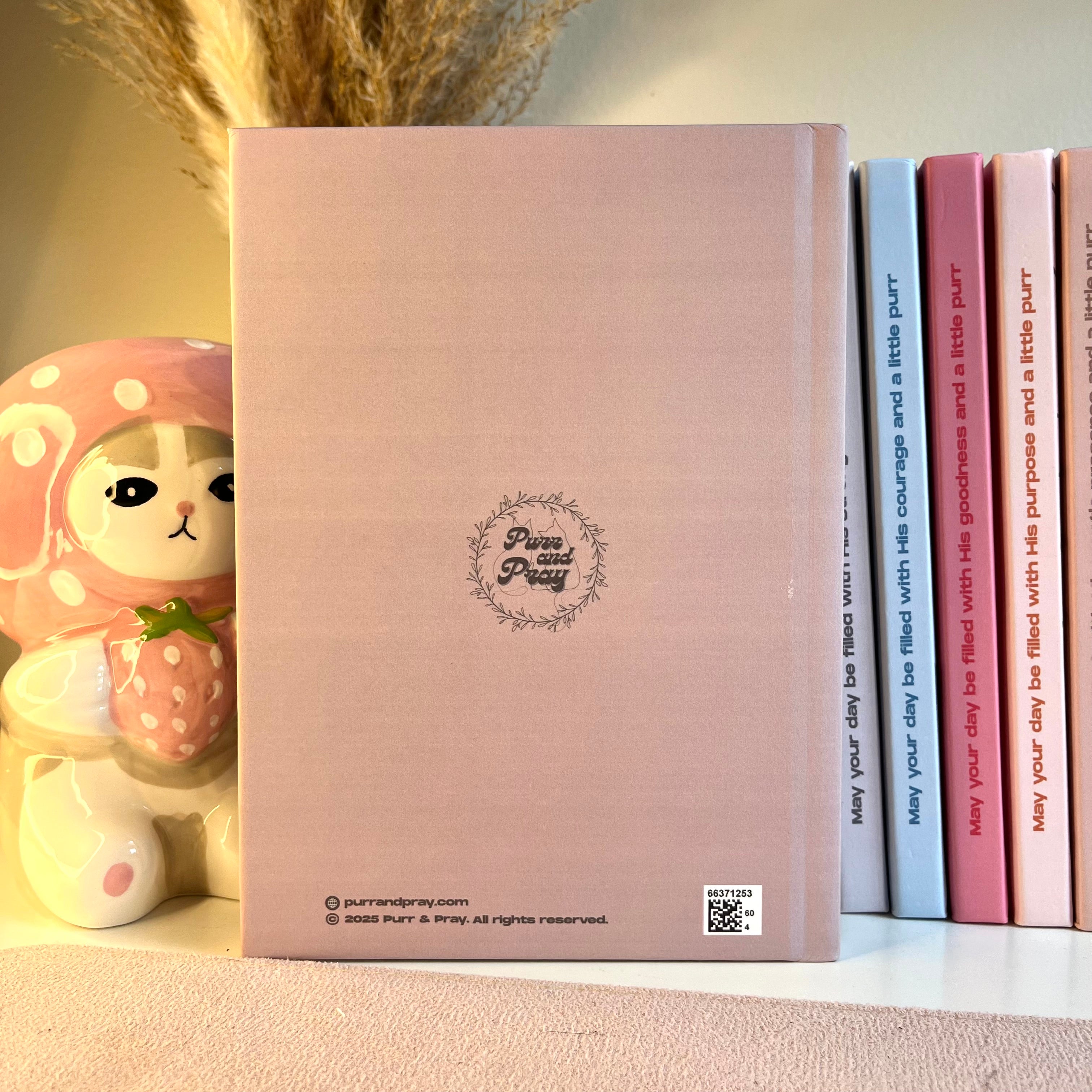 Brown notebook with a brand logo and text, next to a small plush toy, on a light surface.