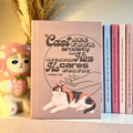 Brown notebook with a calico cat illustration and motivational Bible quote on a shelf with decorative items.