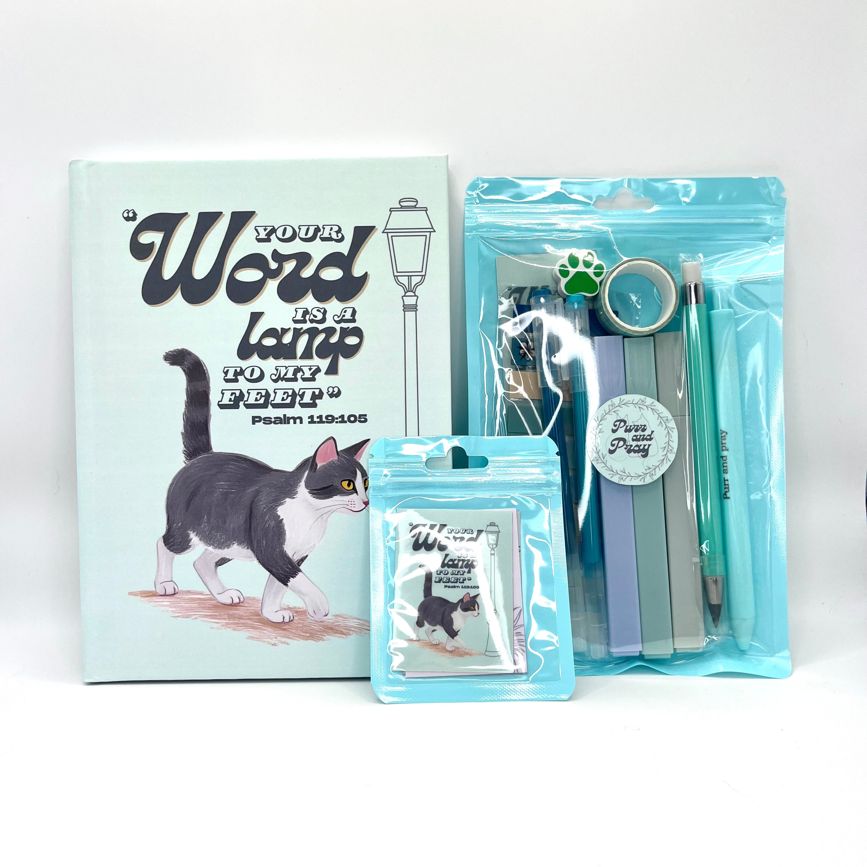 Packaged Christian gift set including a Bible verse journal with a gray tuxedo cat artwork, stationery items in clear bags, and Scripture sticker pack.