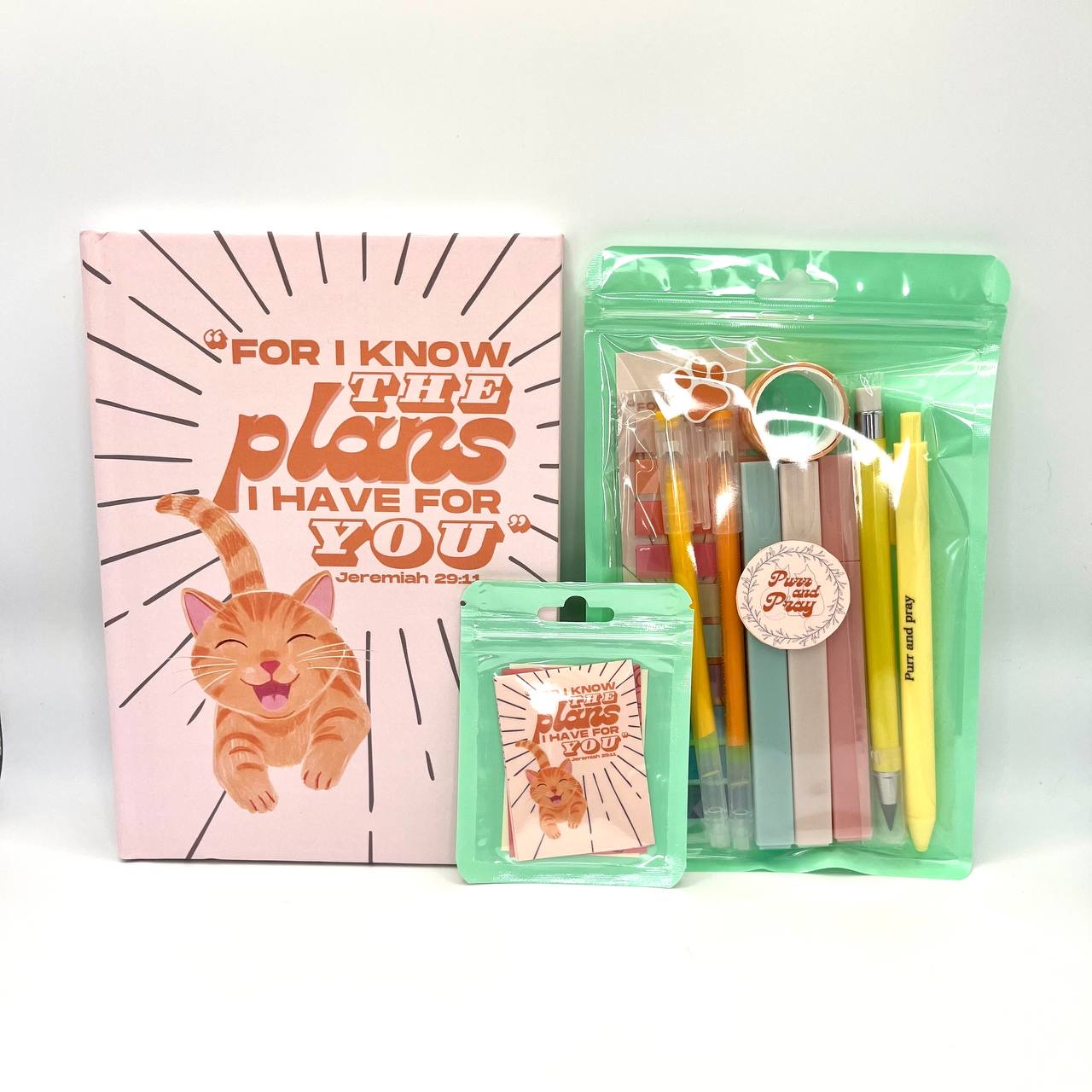 Packaged Christian gift set including a Bible verse journal with orange tabby cat artwork, stationery items in clear bags, and Scripture sticker pack.