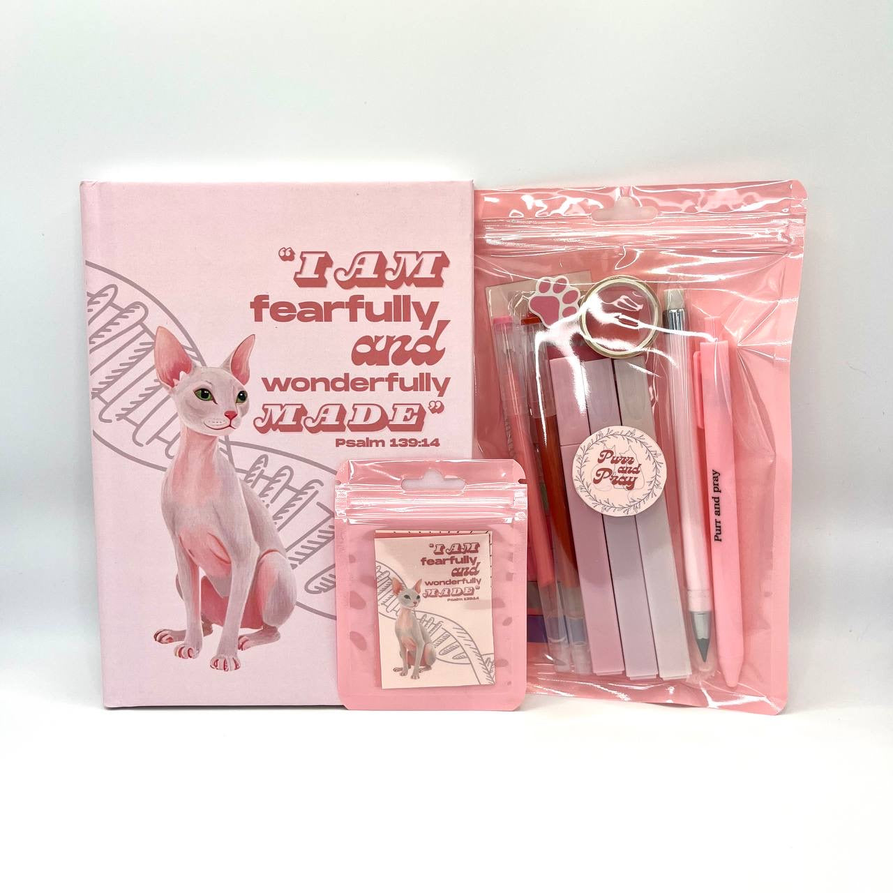 Packaged Christian gift set including a Bible verse journal with a sphynx cat artwork, stationery items in clear bags, and Scripture sticker pack.