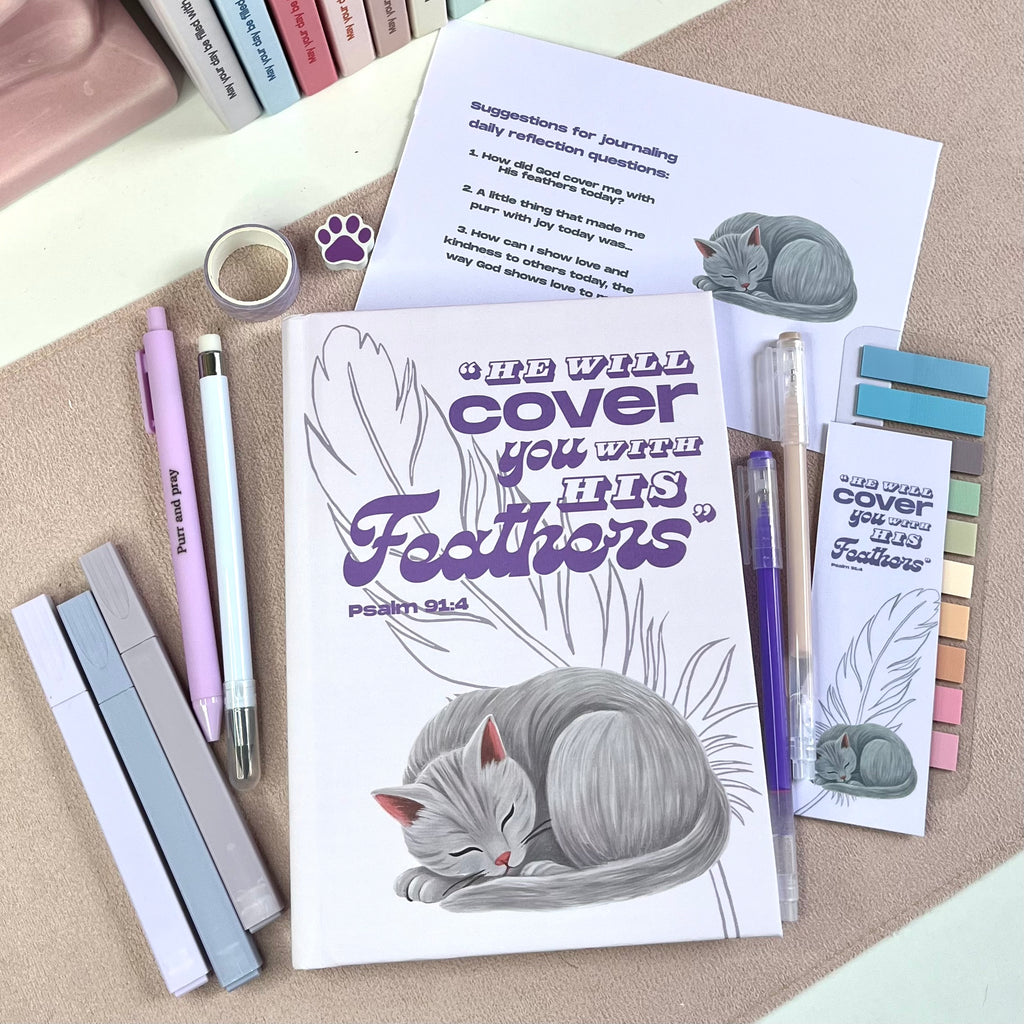 Notebook with a gray cat illustration and text, surrounded by pens and bookmarks on a textured surface.
