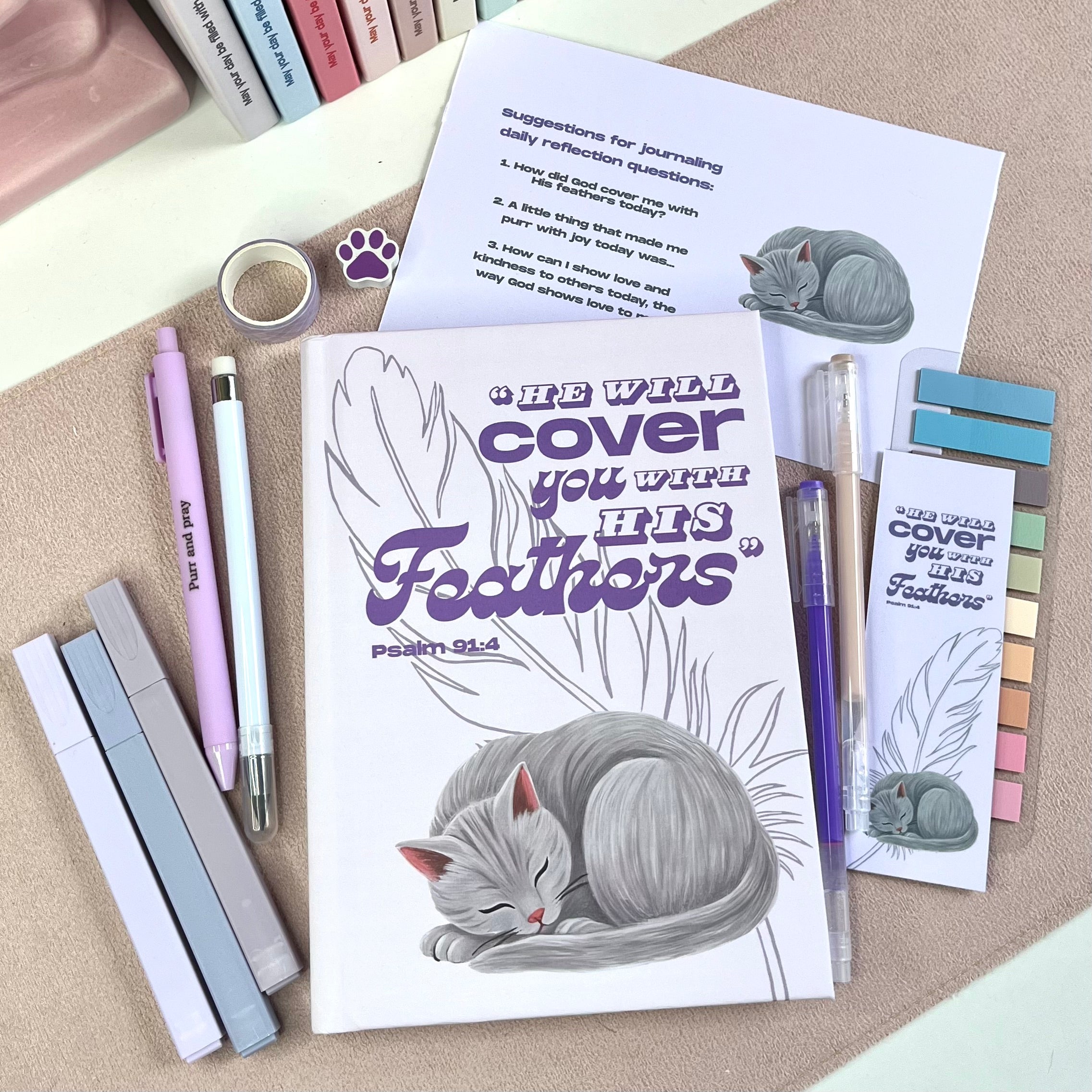 Notebook with a gray cat illustration and text, surrounded by pens and bookmarks on a textured surface.