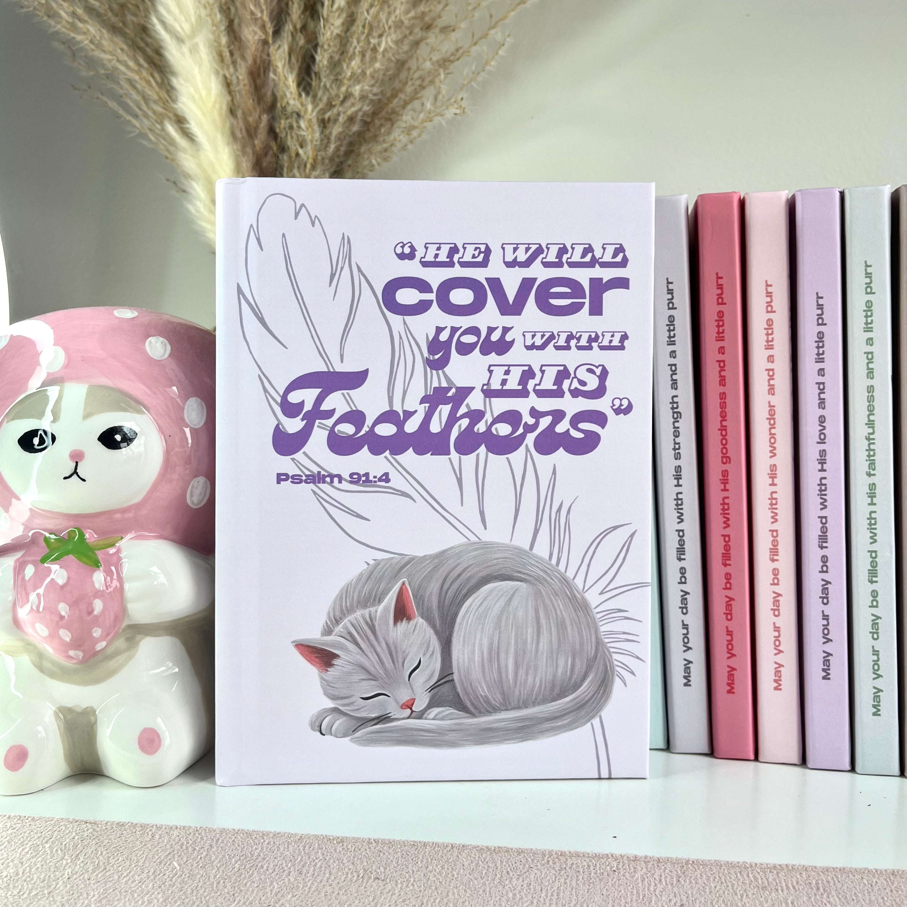 Lavender color book with a gray cat illustration and Bible verse text on a shelf with decorative items.
