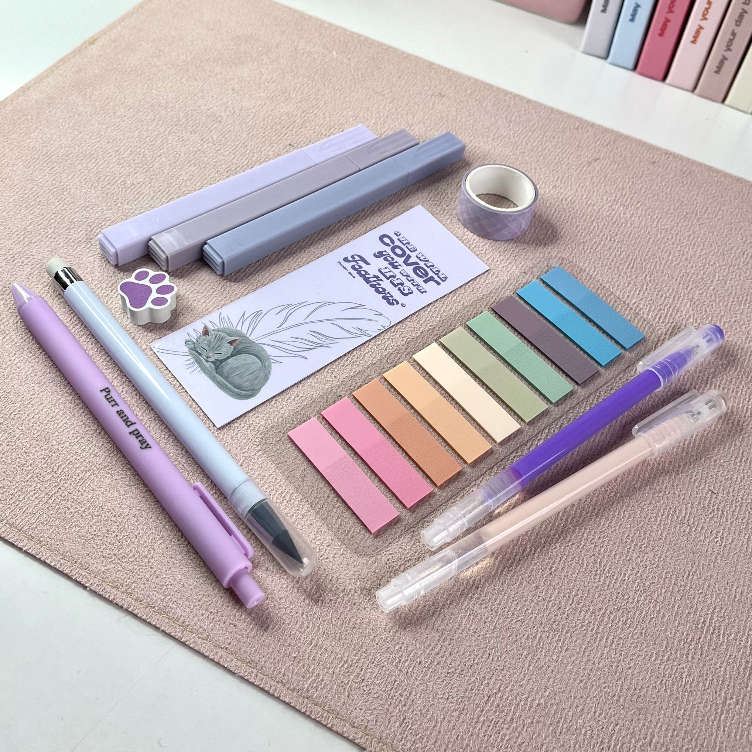 Set of purple stationery items including pens, markers, and color swatches on a textured surface with a gray cat picture.