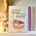 Notebook with a gray tabby cat illustration and motivational Bible quote on a shelf with decorative items.