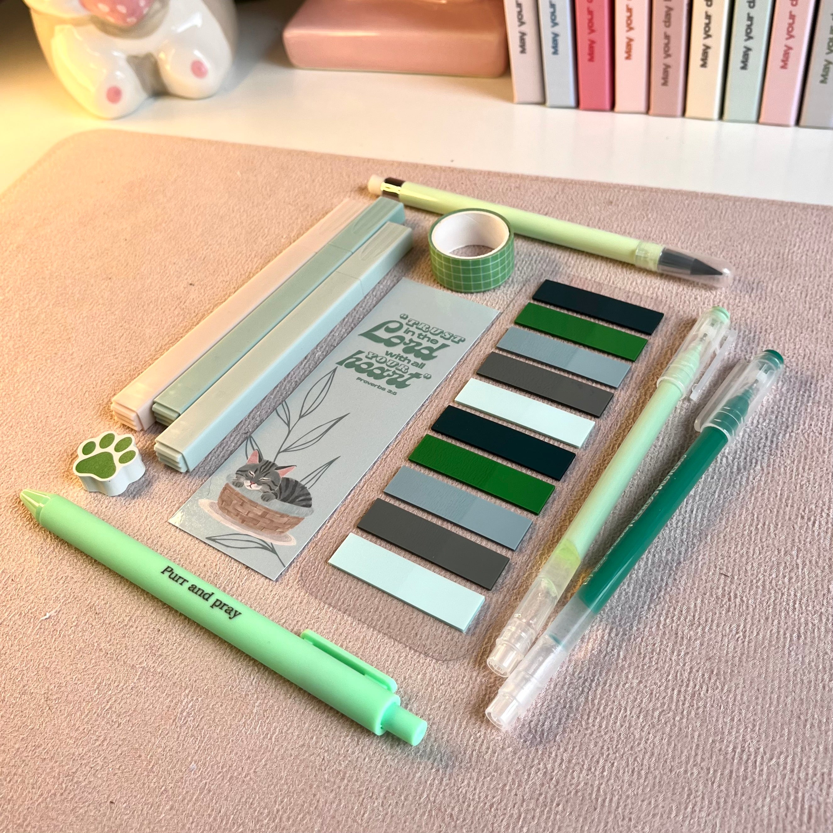 Green stationery items including pens, markers, and a bookmark on a beige surface.