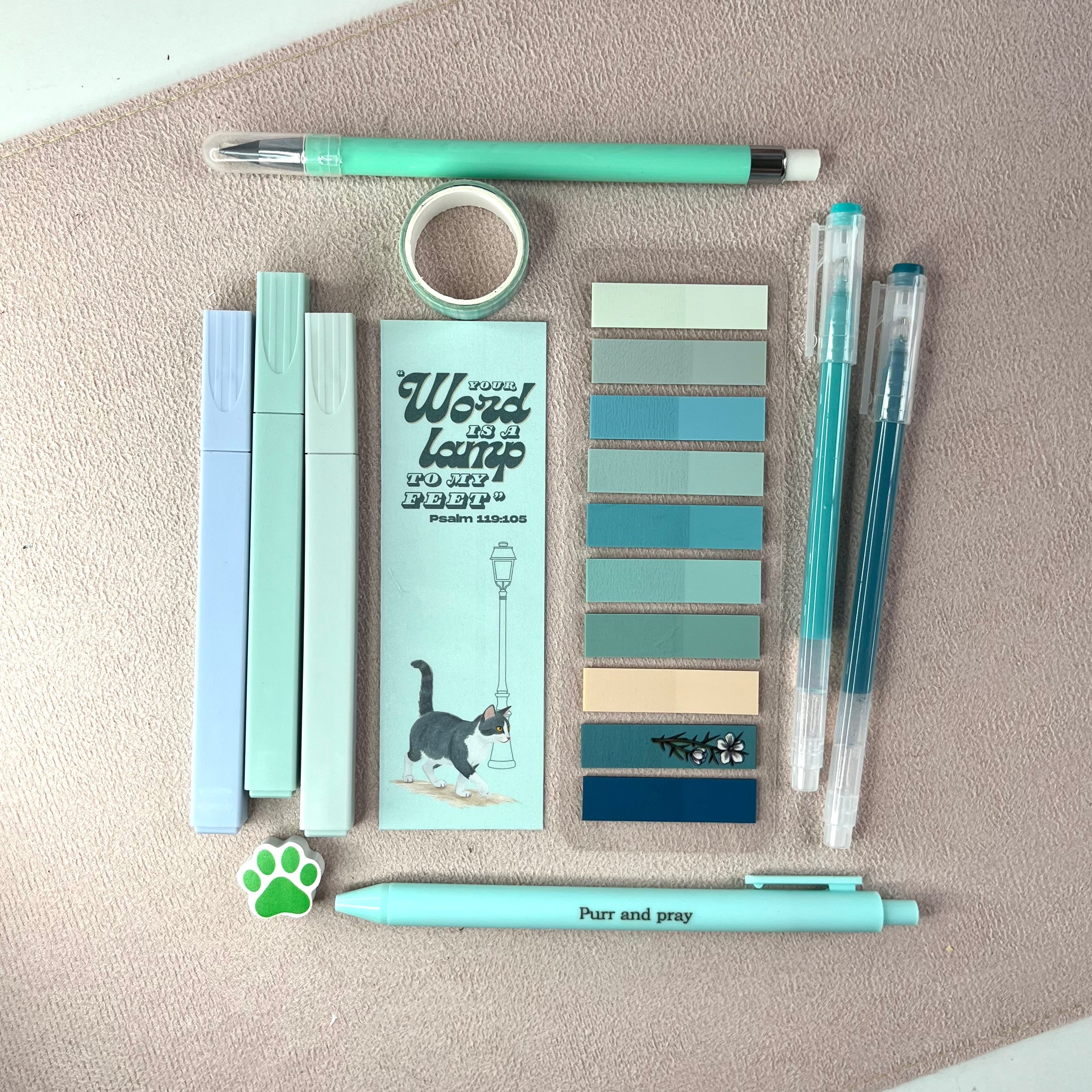 Collection of mint stationery items including pens, markers, and a bookmark on a textured surface.