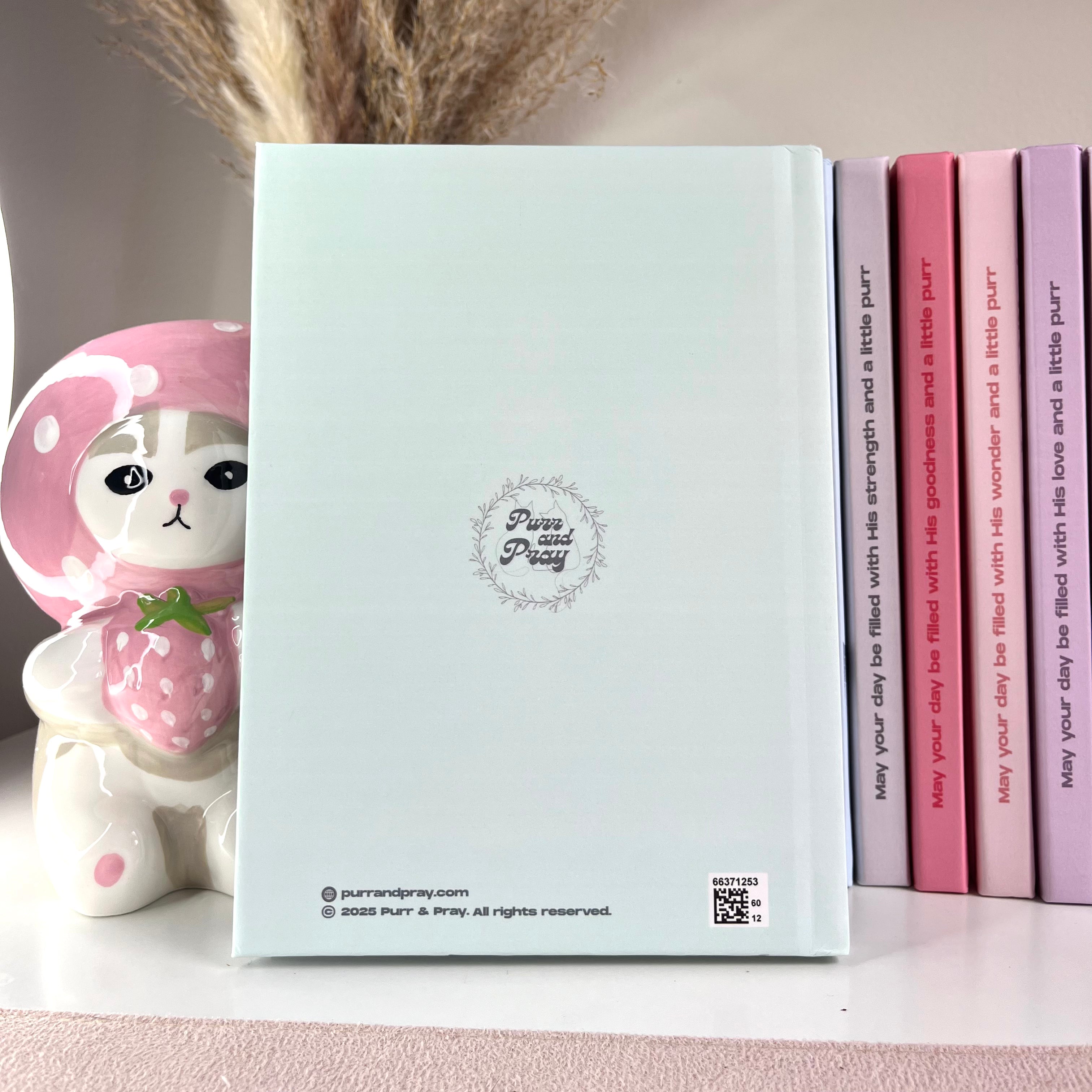 Notebook with a cute design on the cover, placed next to pink and purple books.