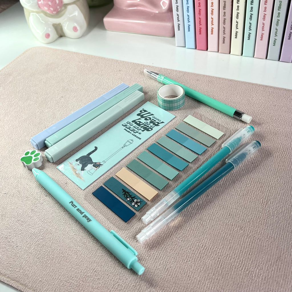 Turquoise stationery items including pens, markers, and washi tape on a textured surface.
