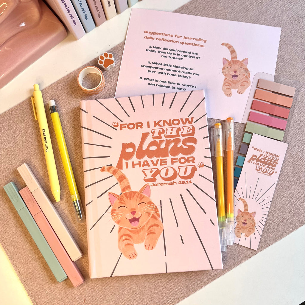 Notebook with orange cat illustration, pens, and stationery items on a textured surface