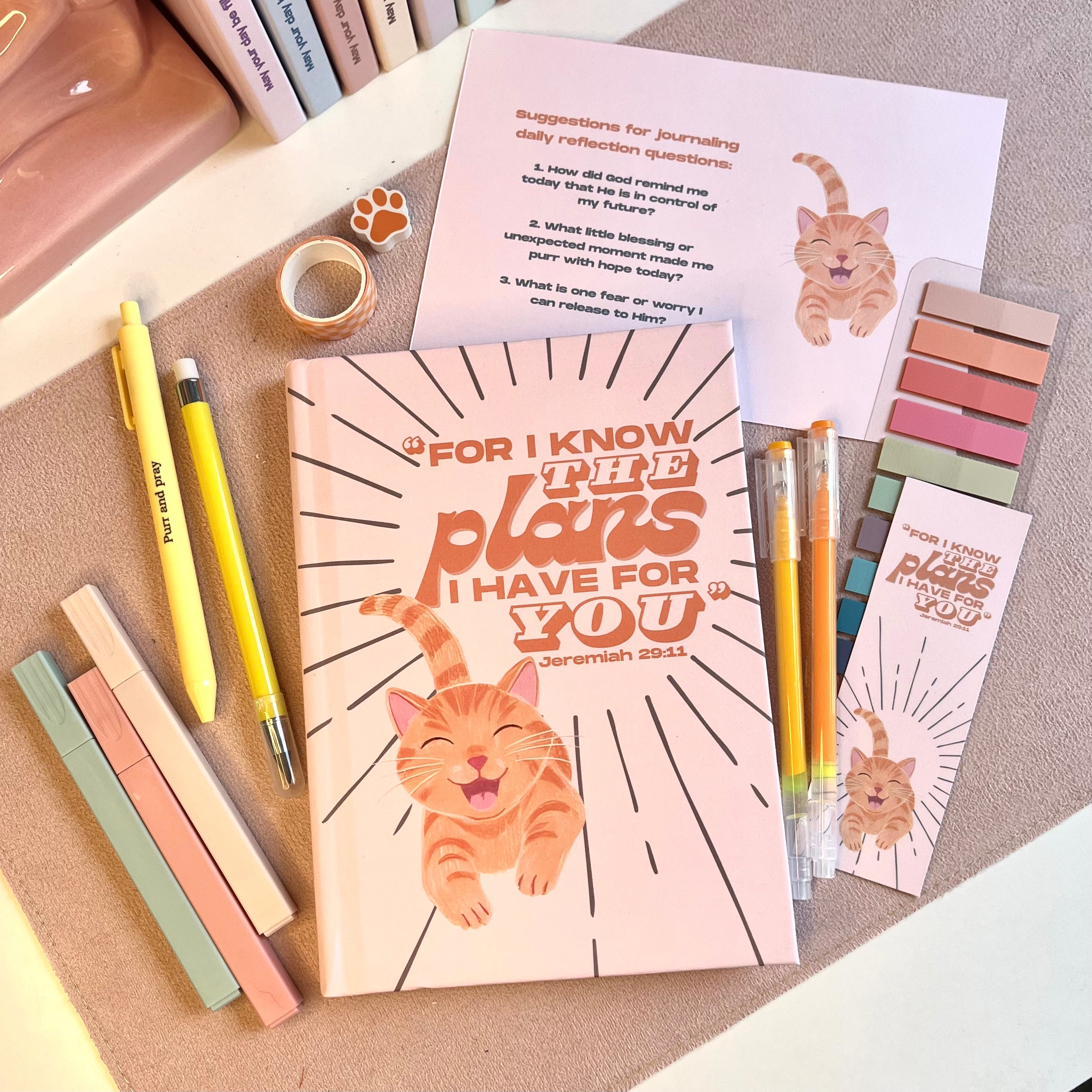 Notebook with orange cat illustration, pens, and stationery items on a textured surface