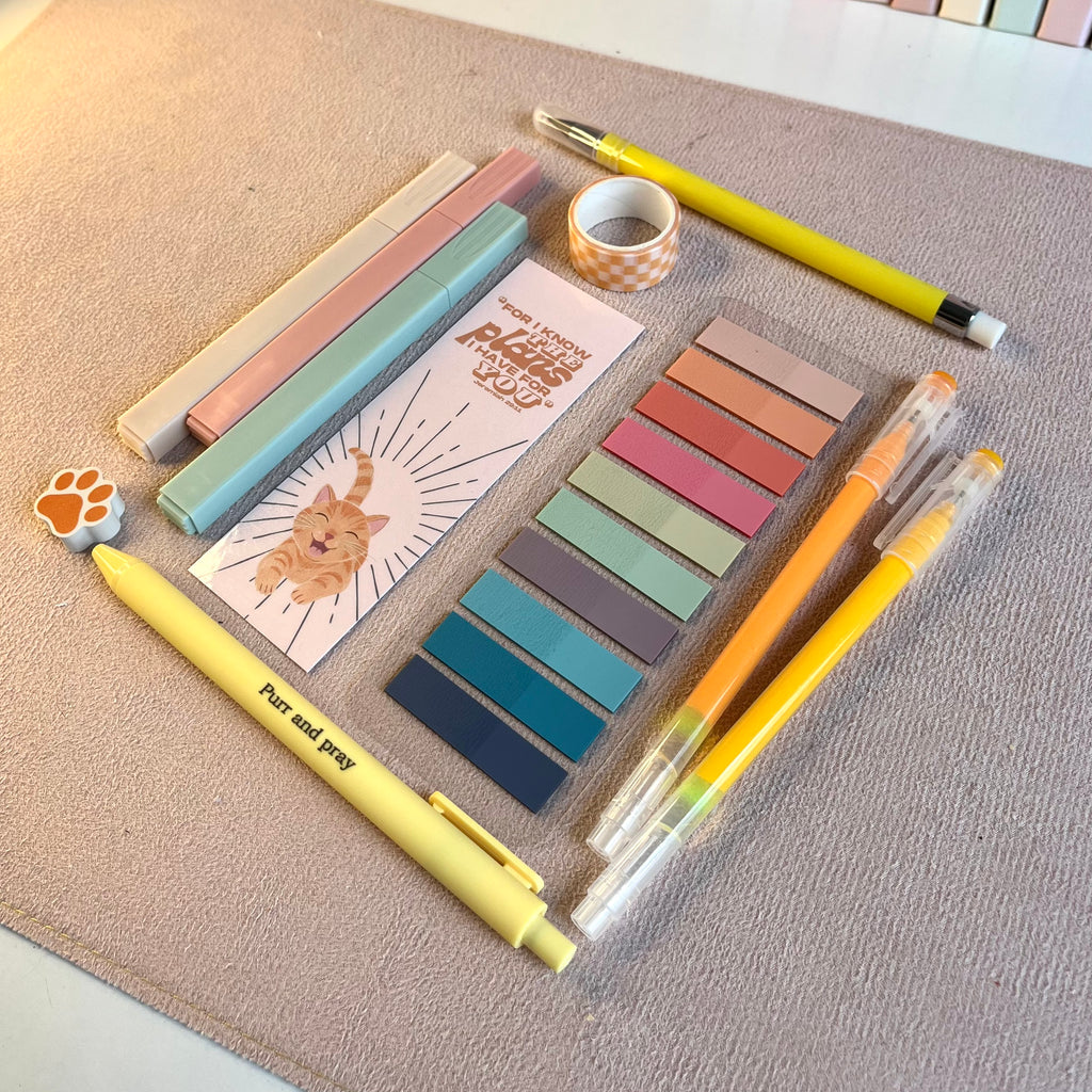 Colorful orange stationery items including pens, markers, and a notebook on a textured surface.