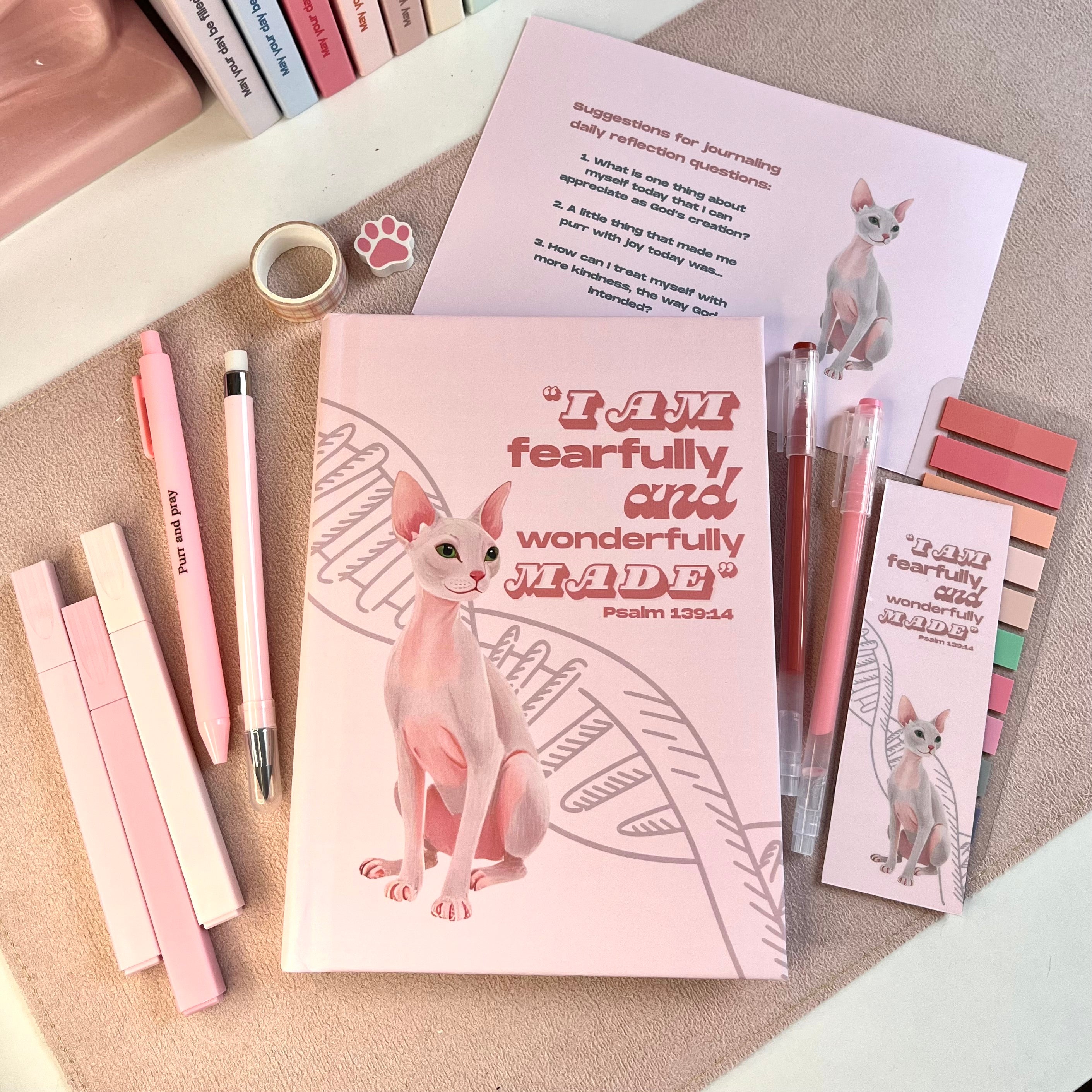 Notebook with sphynx cat illustration and motivational quote on a desk with stationery items.