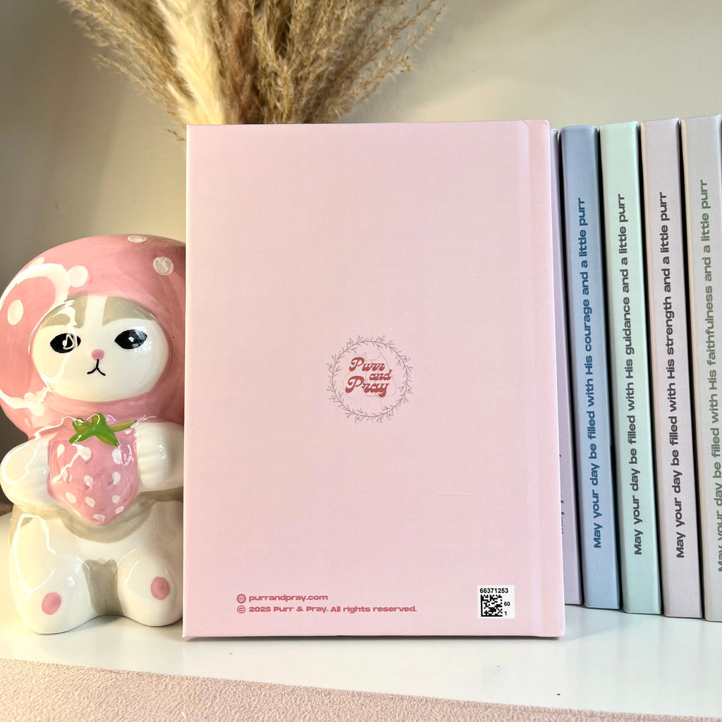 Pink notebook with a cute character design on a shelf with books and decorative items.
