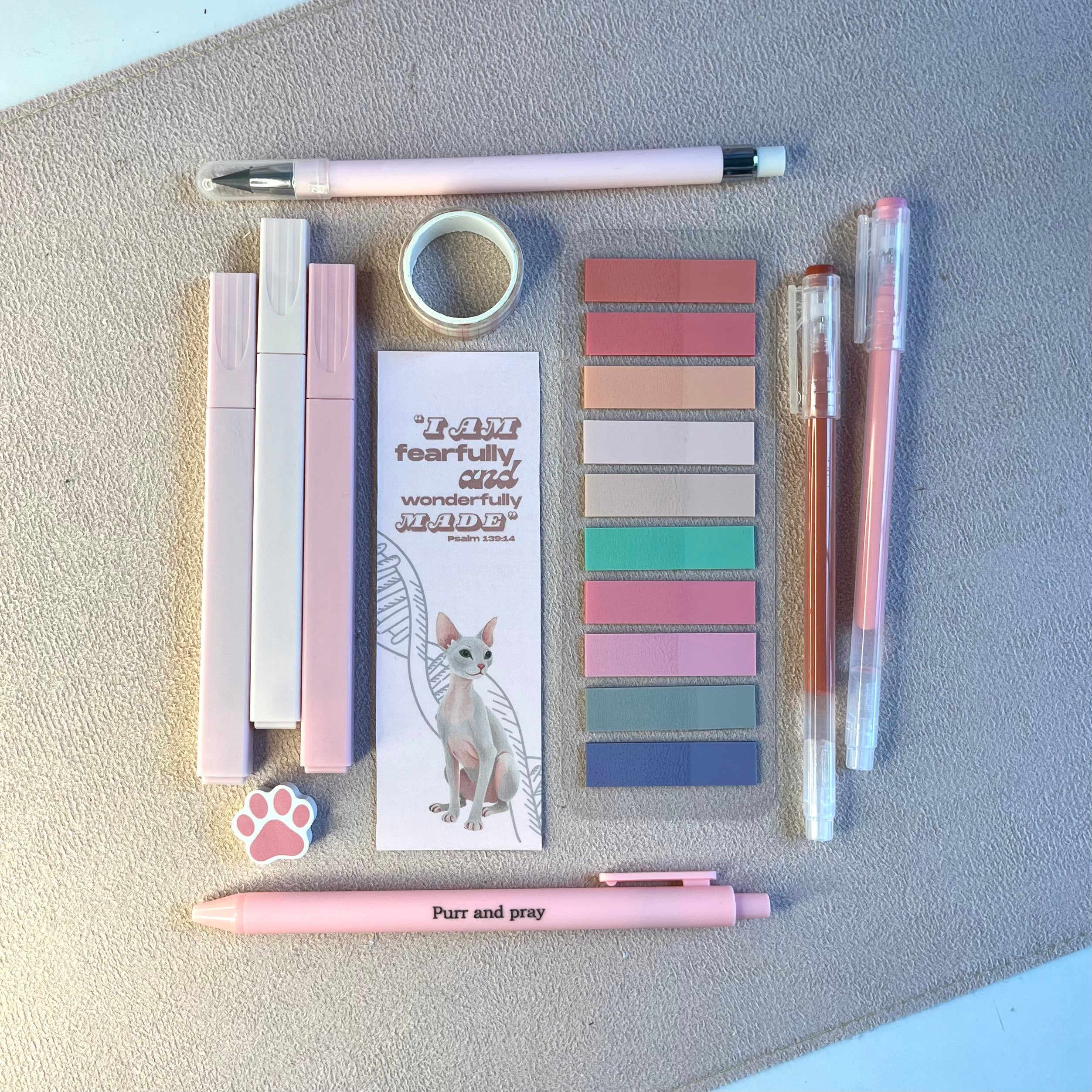 Stationery items including pens, sticky notes, and a bookmark with sphynx cat illustration on a textured surface