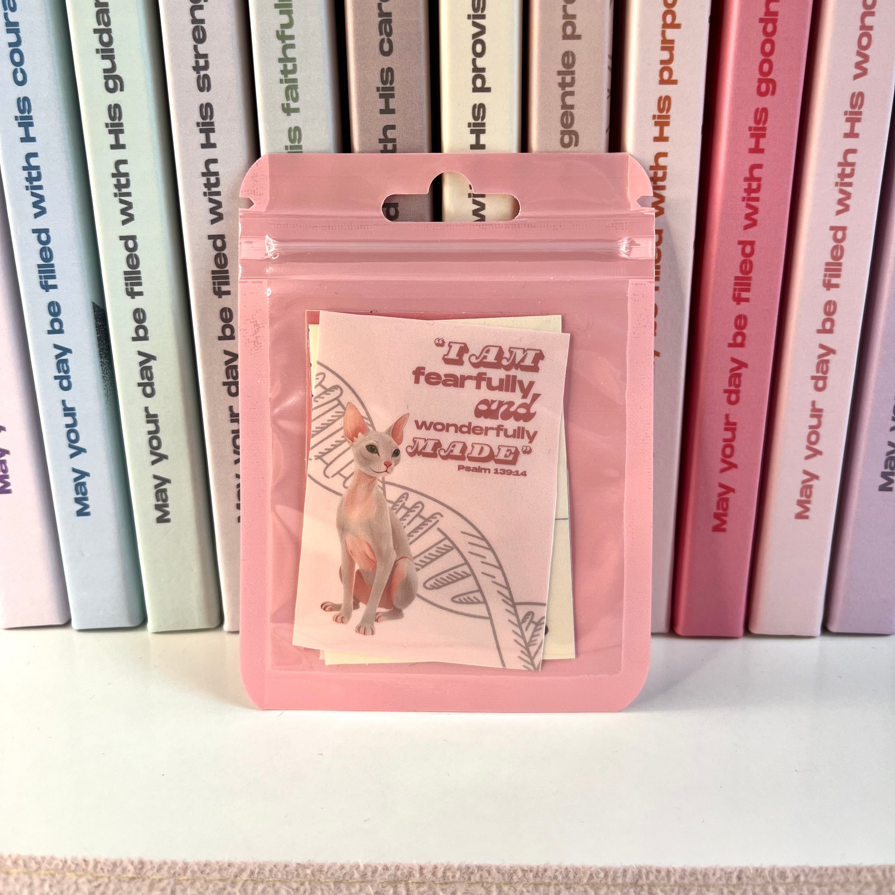 Pink packaging with a cat illustration and text, set against a background of books.