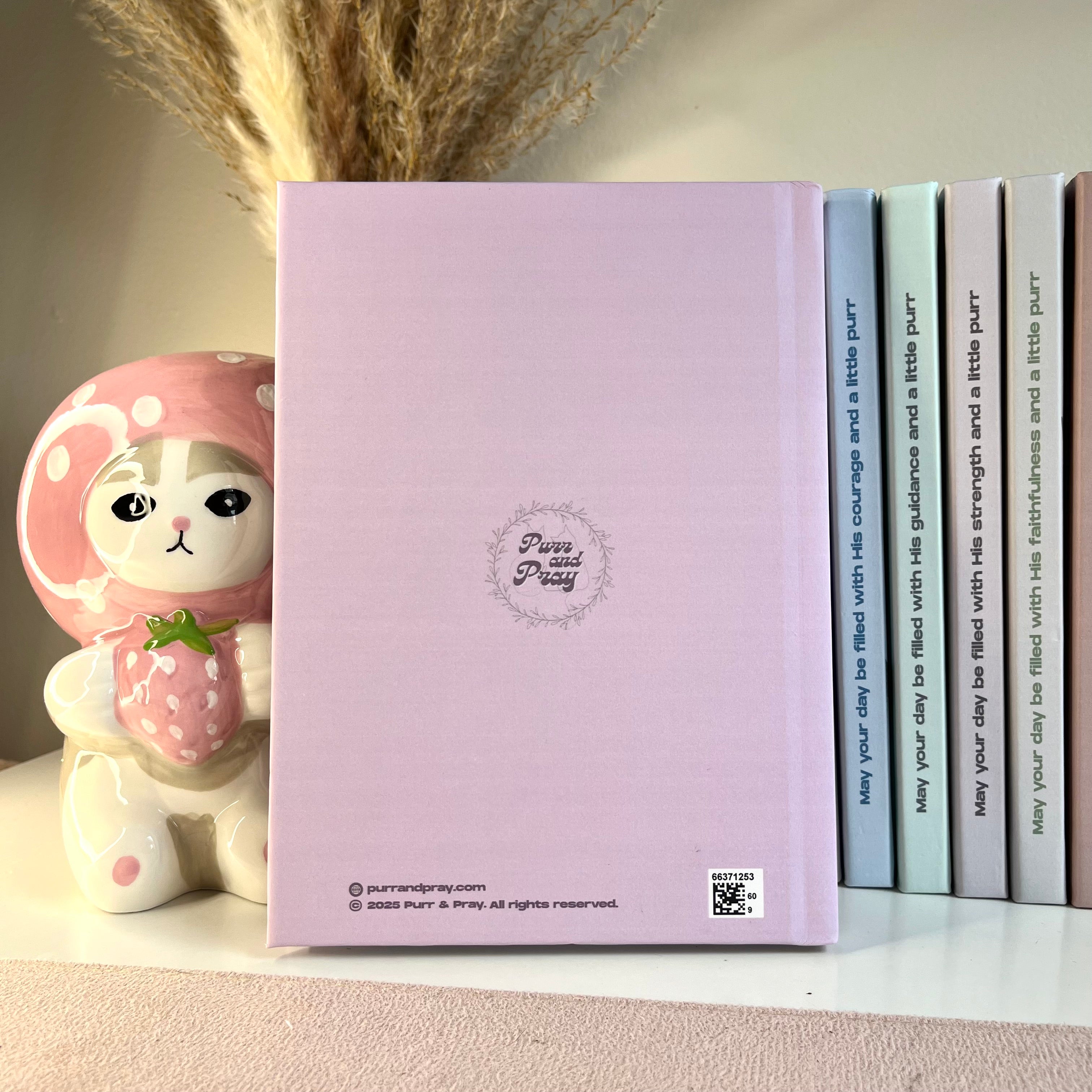 Purple notebook with a cute character design on a shelf with decorative items.