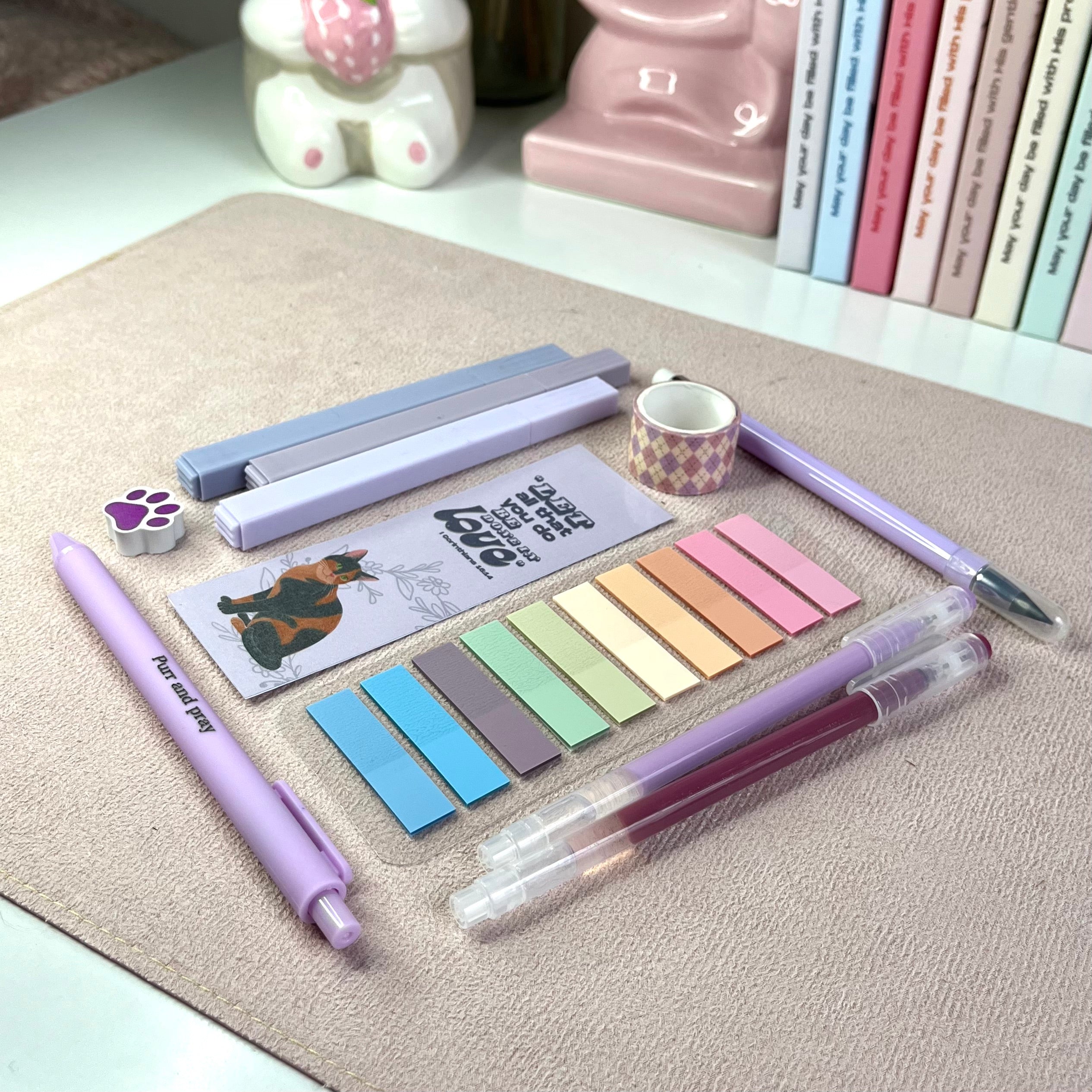 Assorted purple stationery items including pens, sticky notes, and a bookmark on a textured surface.