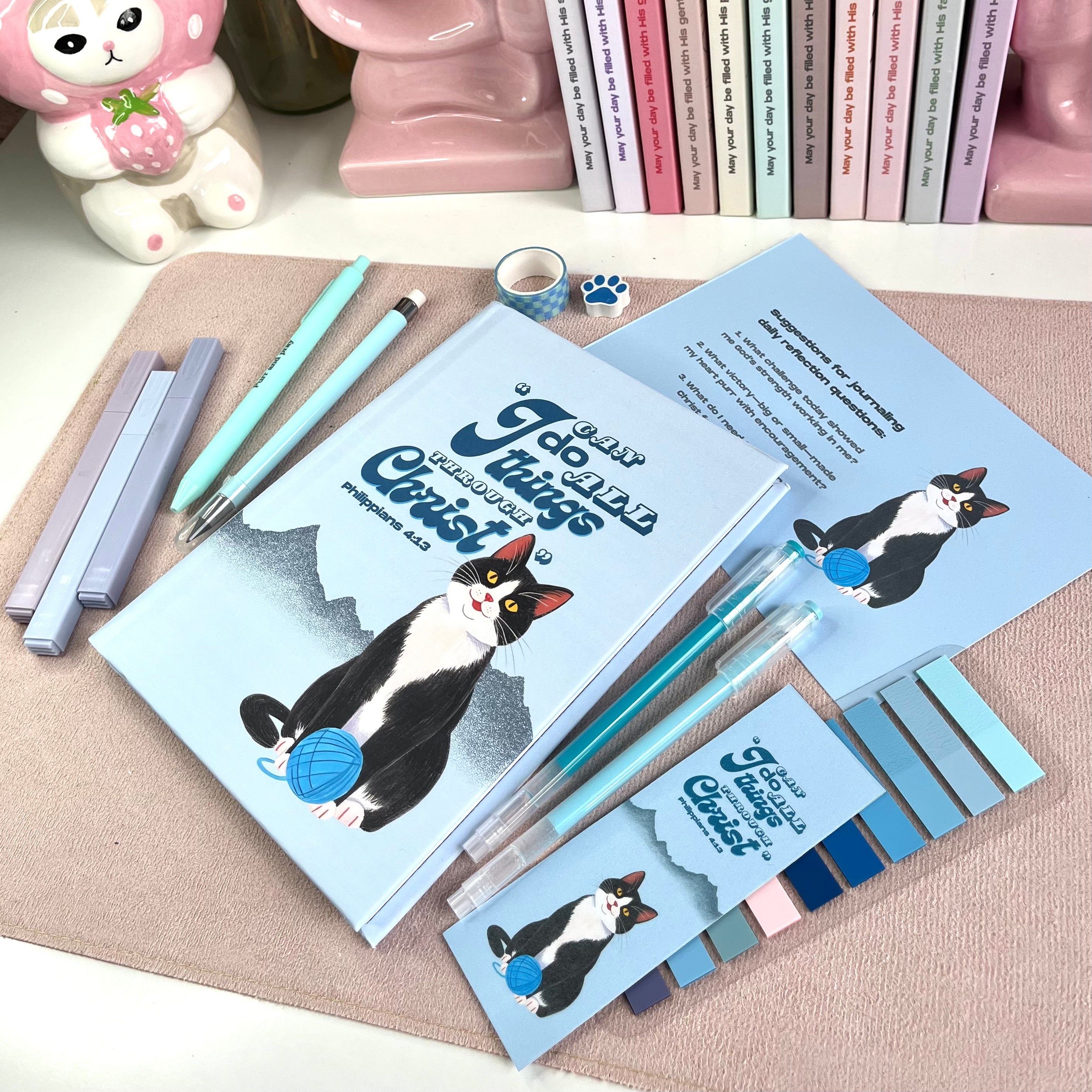 Notebooks and stationery items with a tuxedo cat design on a beige surface.