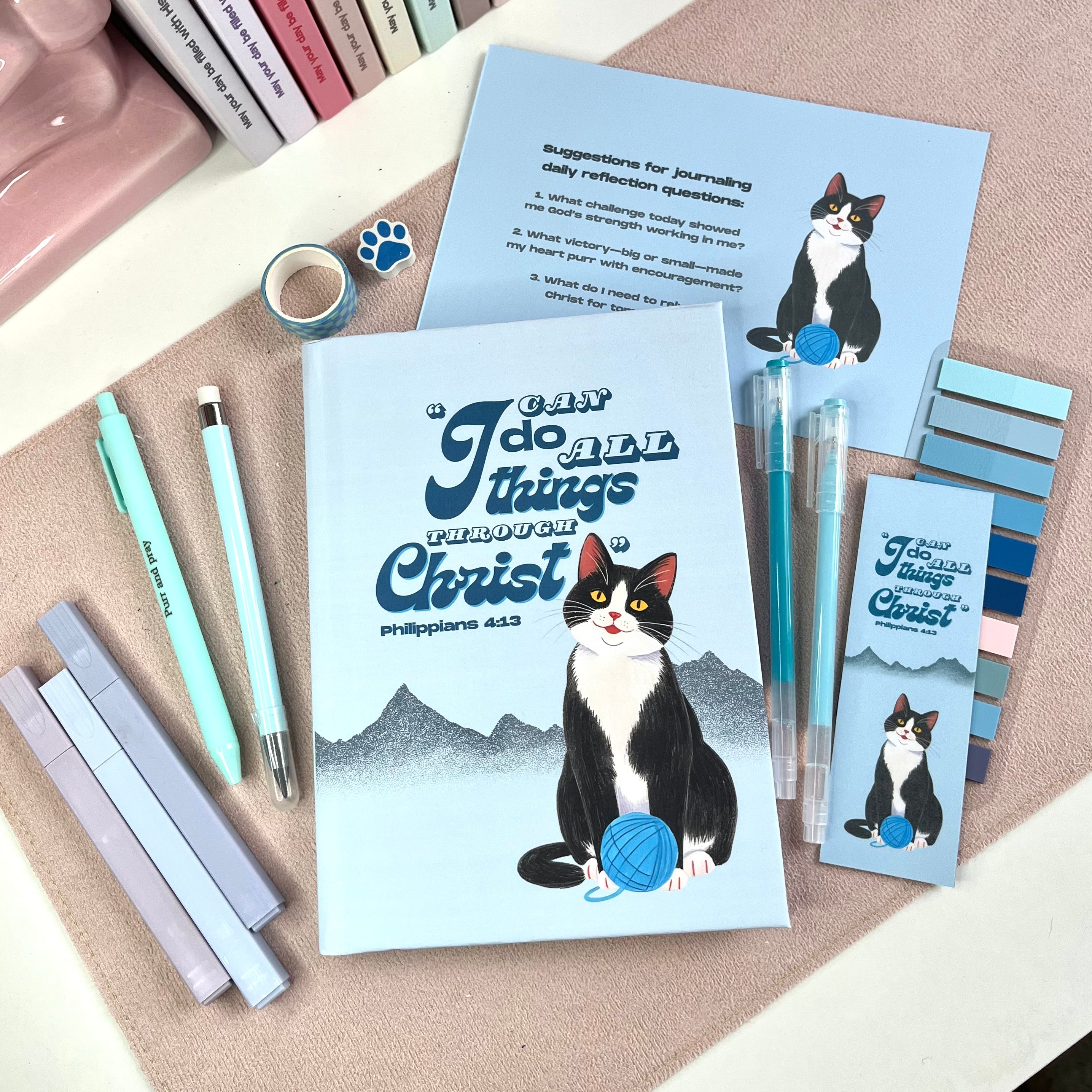Stationery items with tuxedo cat illustrations and motivational text on a textured surface