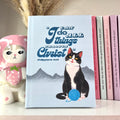 A blue notebook with a tuxedo cat on it and a Bible verse text.